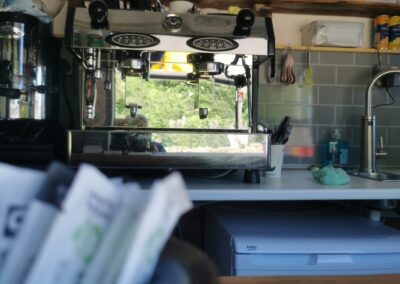 "Espresso machine and grinder in a compact eco-friendly trailer café, with Fairtrade sugar sachets and ethically sourced drinks on shelves."