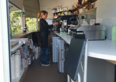 Barista making coffee inside a repurposed trailer café with eco-friendly supplies and a professional espresso machine at bearesden campsite