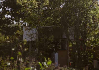 "Trailer café hidden among dense trees and foliage at a quiet eco campsite, with open hatches revealing a coffee setup inside."
