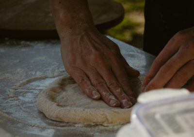 "Close-up of hands shaping fresh pizza dough on a floured work surface in natural light."