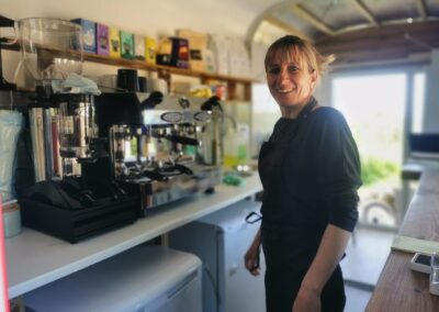 "Smiling barista standing next to an espresso machine in a bright, sustainable trailer café with eco-friendly coffee supplies."